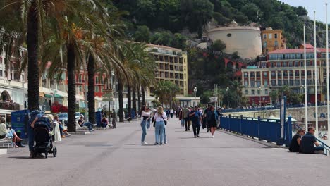 People-Walk-On-Seaside-Street-Quai-des-Etats-Unis-In-Nice,-France-by-Colline-du-Chateau,-wide-shot