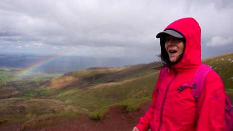 Excited-woman-pointing-a-colorful-rainbow-after-the-rain-in-Brecon-Beacons-National-Park,-Wales