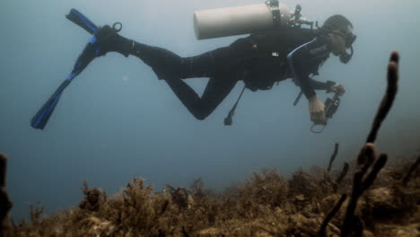 Underwater-shot-of-a-diver-holding-a-camera-while-swimming-in-a-Caribbean-reef