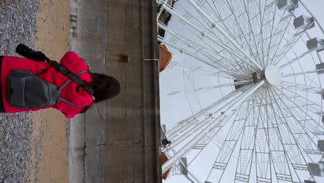 Still-rear-view-of-a-woman-on-a-rocky-beach-facing-a-ferris-wheel-in-The-Mumbles,-Wales