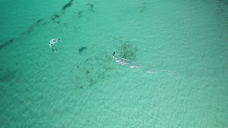 Kite-surfer-gliding-over-turquoise-waters-near-sandy-shore,-aerial-view