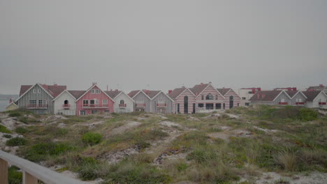 Colorful-striped-houses-at-Praia-da-Costa-Nova-in-Aveiro,-Portugal,-with-sand-dunes-in-the-foreground