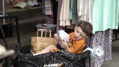 Cute-Boy-Toddler-In-Stroller-Having-Fun-Playing-Bubble-Gun-Toy-At-50th-Dogwood-Festival-In-Siloam-Springs,-Arkansas