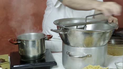 Chef-uses-hand-mixer-to-grind-and-press-mixture,-spinning-metal-handle-next-to-boiling-pot-of-water