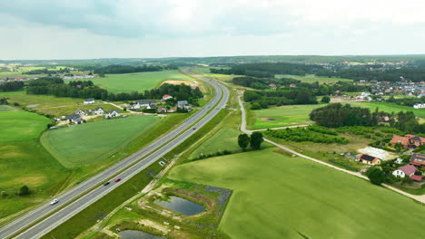 Vista-Aérea-De-Una-Carretera-Rural-Cerca-De-Gdynia,-Rodeada-De-Vastos-Campos-Verdes-Y-Casas-Dispersas,-Capturando-La-Tranquilidad-Y-El-Espacio-Abierto-Del-Paisaje-Rural