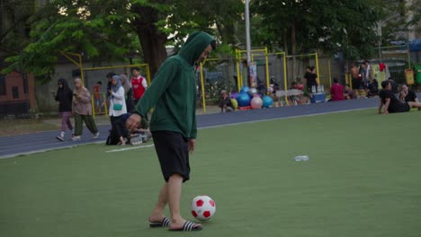 Man-in-hoodie-running-and-playing-soccer-on-colorful-urban-playground-with-other-people-in-the-background