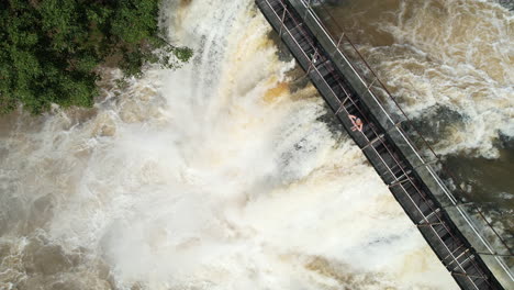 Aerial-View-of-Woman-Standing-on-Footbridge-Above-Scenic-Mena-Creek-Falls,-Queensland,-Australia