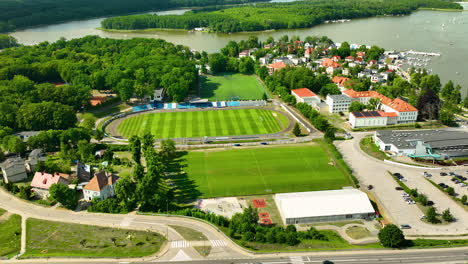 Vista-Aérea-De-Iława-Con-Un-Estadio-De-Fútbol,-Exuberante-Vegetación,-Zonas-Residenciales-Y-Un-Lago,-Destacando-Los-Servicios-Paisajísticos-Y-Recreativos-De-La-Ciudad.