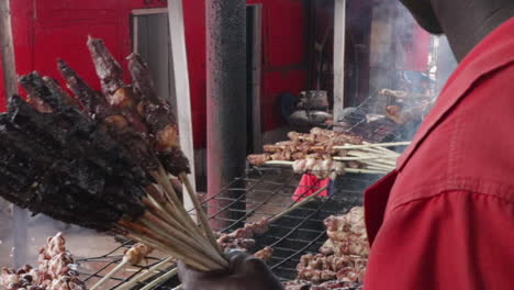 Hombre-Africano-Cocinando-Brochetas-De-Carne-A-La-Parrilla-En-Un-Mercado-En-Uganda,-África