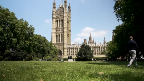 Black-bald-professional-man-walking-across-a-green-park-near-Westminster-with-architectural-buildings-in-the-background