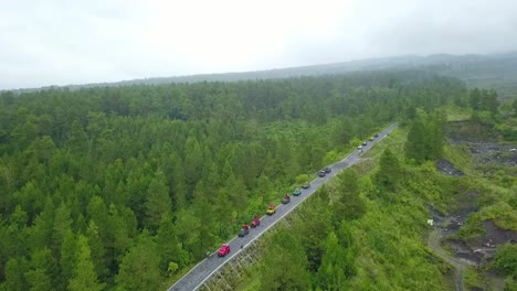 Aerial-view-of-car-vehicles-crossing-a-green-forest-road,-Jeep-trip-on-the-green-rain-forest-on-the-slope-of-mountain