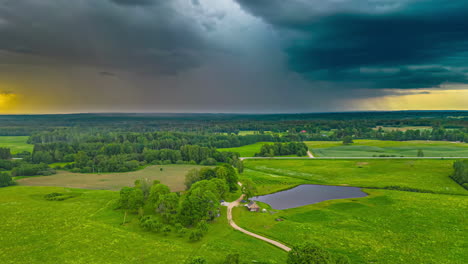 Dark-Cloudscape-Over-Rural-Meadow-Landscape-With-Small-Pond-And-Houses