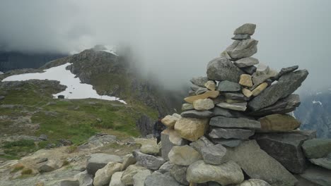 Two-hikers-explore-the-rocky-and-misty-Litlefjellet-trail-in-Norway,-surrounded-by-towering-cairns