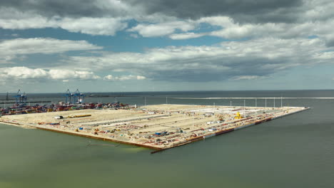 Aerial-view-of-construction-work-at-the-Port-of-Gdańsk,-showcasing-an-extensive-dockyard-with-cranes-and-industrial-equipment,-set-against-the-backdrop-of-the-Baltic-Sea