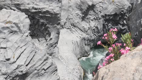 Water-flows-between-big-grey-stones-in-the-river,-showing-a-beautiful-view-in-Taormina