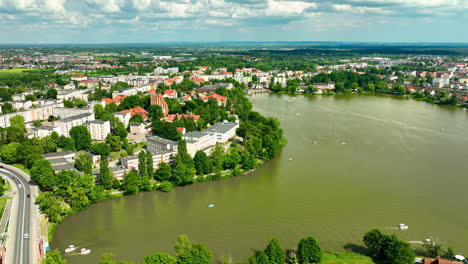 Aerial-view-of-Iława,-showing-the-town-by-a-large-lake-with-surrounding-greenery-and-buildings-under-a-partly-cloudy-sky