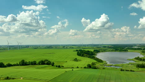 Ausgedehnte-Grüne-Felder-Mit-Windrädern-Und-Einem-See-Unter-Einem-Strahlend-Blauen-Himmel-Mit-Flauschigen-Wolken