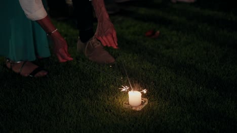 Encendiendo-Bengalas-Cerca-De-Una-Vela-En-Un-Césped-Durante-Un-Evento-Nocturno