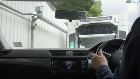 Man-pulls-car-up-to-entrance-of-automated-car-wash-facility,-POV-from-inside-car