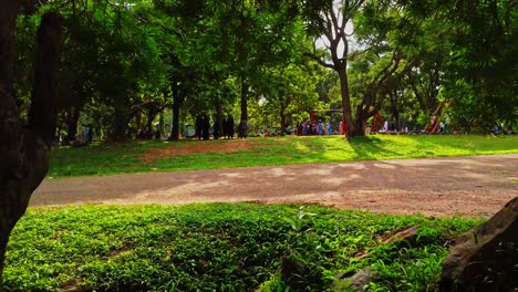 The-camera-slowly-moves-between-trees-towards-a-busy-children's-play-park-in-a-beautiful-park-in-Abuja,-Nigeria