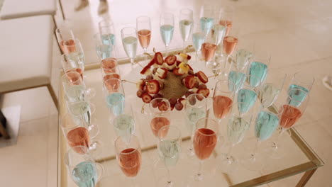 table-with-an-arrangement-of-blue-and-pink-cocktails-in-champagne-flutes,-surrounding-a-centerpiece-of-skewered-fruit-pieces