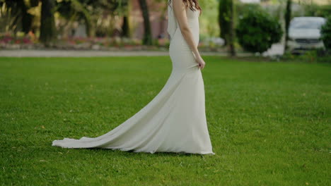 Bride-in-a-flowing-white-dress-walking-gracefully-on-green-grass-in-a-serene-park