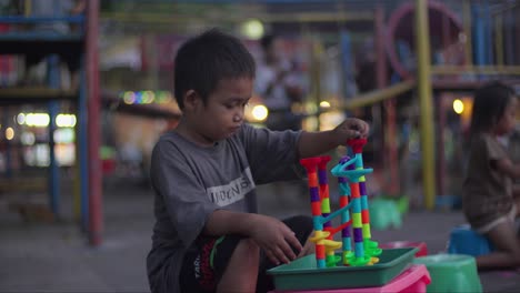 Boy-playing-with-colorful-toy-marble-run-in-outdoor-playground-during-evening