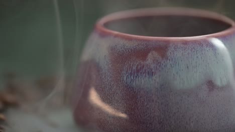 Macro-De-Un-Humo-Se-Desplaza-Sobre-La-Taza-Lila,-Taza-Rodeada-De-Granos-De-Café-Sobre-La-Mesa