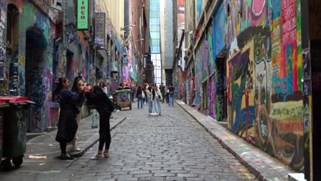 Visitors-walking-through-popular-Hosier-Lane,-a-cobblestone-laneway-with-a-vibrant-array-of-art-murals-and-graffiti-on-the-walls,-a-creative-cultural-street-scene-in-Melbourne-city