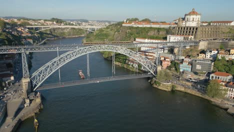 4K-Drohnenaufnahme-Der-Don-Luis-I-Brücke-Im-Historischen-Zentrum-Von-Porto-Bei-Sonnenuntergang,-Während-Ein-Zug-Darüber-Und-Ein-Boot-Darunter-Hindurchfährt