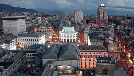 Twilight-aerial-dolly-toward-illuminated-Piazza-de-Ferrari-in-Genova-city