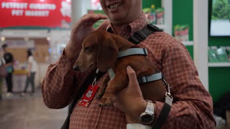 Hombre-Sujetando-Un-Pequeño-Perro-Salchicha-En-Un-Festival-De-Mascotas-En-Indonesia