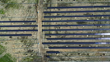 Aerial-drone-top-down-shot-flying-high-over-newly-constructed-solar-panels-along-rural-countryside-on-a-sunny-day