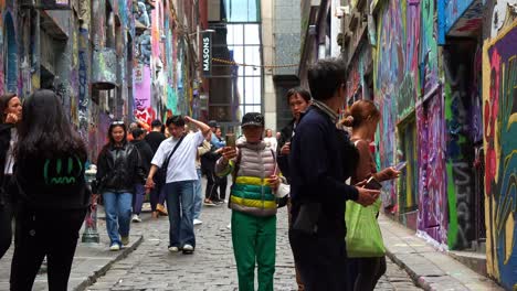 People-walking-through-Hosier-Lane,-a-popular-cobblestone-laneway-with-a-vibrant-array-of-art-murals-and-graffiti-on-the-walls,-a-creative-cultural-street-scene-in-Melbourne-city,-Victoria