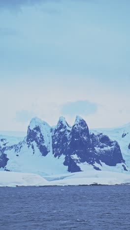 Sunset-Snowcapped-Winter-Mountains-Coastal-Scenery-in-Antarctica,-Snowy-Snow-Covered-Landscape-on-the-Coast-of-Antarctic-Peninsula-in-Vertical-Video-for-Social-Media,-Instagram-Reels-and-Tiktok