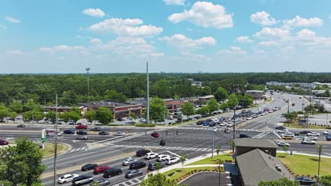 Aerial-approaching-shot-of-traffic-on-junction-with-shopping-mall-and-forest-in-background