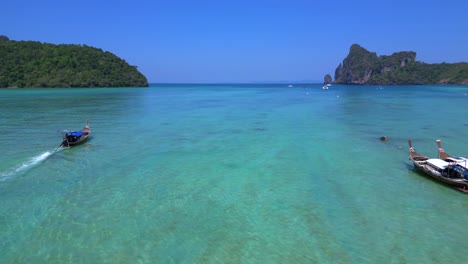 Koh-Phi-Phi-Bay,-colorful-traditional-longtail-boats-are-floating-on-calm-turquoise-water