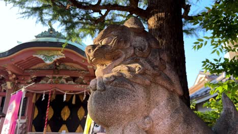 Steinerne-Löwenstatue-In-Einem-Japanischen-Tempel-Unter-Einem-Baum-An-Einem-Sonnigen-Tag