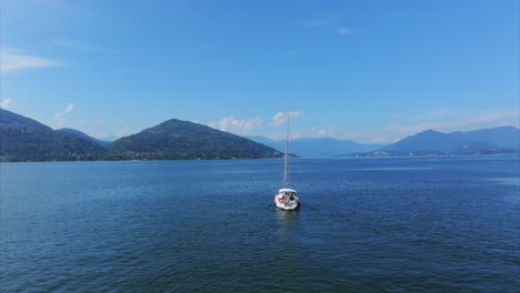 Luftaufnahme-Eines-Einsamen-Segelboots-Inmitten-Eines-Ruhigen,-Ausgedehnten-Gewässers-Mit-üppigen-Grünen-Bergen-Im-Hintergrund-Unter-Einem-Klaren-Blauen-Himmel