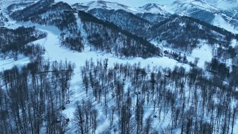 Una-Vista-Aérea-De-Un-Complejo-De-Montaña-Nevado,-Con-Remontes-Y-Picos-Nevados-Al-Fondo