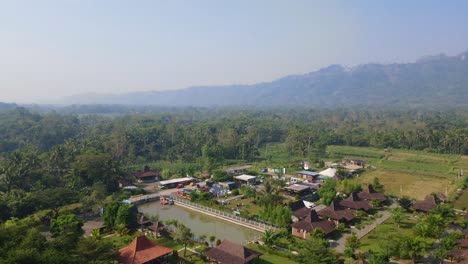 Aerial-view-of-"Balkondes-Wanurejo"-and-Junkyard-Park-with-colorful-card-parking-on-the-yard-in-sunny-morning-and-hills-on-the-background