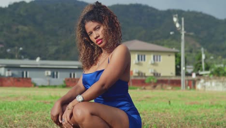 A-curly-haired-girl-squat-in-the-grass-in-a-short-blue-dress-enjoys-a-tropical-park-in-Trinidad