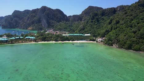 Türkisfarbenes-Wasser-Plätschert-Sanft-An-Die-Küste-Einer-Tropischen-Insel,-Mit-Booten,-Die-Die-Meereslandschaft-Und-Die-üppigen-Grünen-Hügel-Säumen