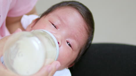 Schläfriges-Neugeborenes-Saugt-Etwas-Milch-Aus-Einer-Babyflasche,-Mit-Der-Es-Gefüttert-Wird,-Während-Es-In-Den-Armen-Seiner-Mutter-Einschläft