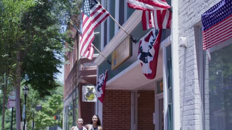 Couple-walking-in-downtown-Fredericksburg,-Virginia-with-slow-motion-tilt-up-to-American-flags-flying-in-slow-motion