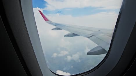 Ventana-Del-Avión-Que-Muestra-Muchas-Nubes-Diferentes-Y-Un-Cielo-Fresco-Con-Un-Silbido-Debajo