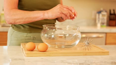 A-medium-close-up-of-a-mother-cracking-eggs-into-a-bowl-in-a-modern-kitchen