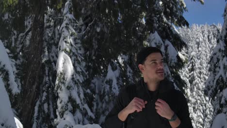 Young-Man-With-Backpack-Hikes-In-The-Mountain-With-Snowy-Forest-On-A-Sunny-Day