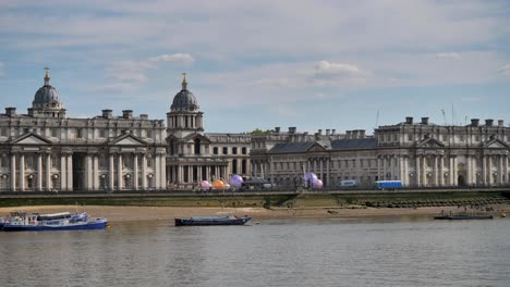 Riverside-view-of-the-Old-Royal-Naval-College-along-the-Thames-with-boats-in-Greenwich,-London,-UK,-July-2023