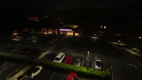 Aerial-approaching-shot-of-hospital-with-emergency-sign-at-night